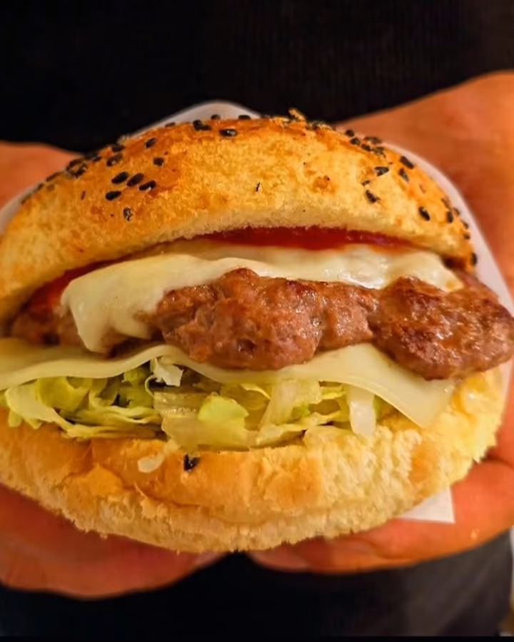 Burger z wołowiną i serem trzymany w dłoniach